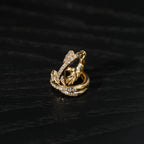 A pair of gold-plated crossover hoop earrings studded with zircon stones, displayed on a dark background.