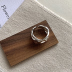 A sterling silver ring with an irregular pleated design, displayed on a wooden surface.